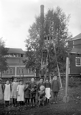 Barn i olika åldrar står framför en industribyggnad, foto i svarttvitt 
