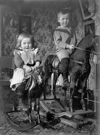 En flicka och en pojke sitter på var sin gunghäst, svartvitt foto